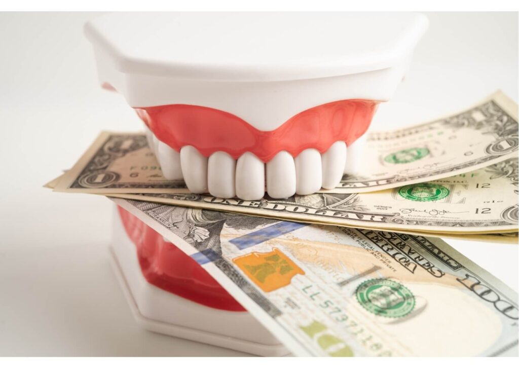 Full denture model placed on U.S. dollar bills representing the cost of dental implants and restorative dental treatment