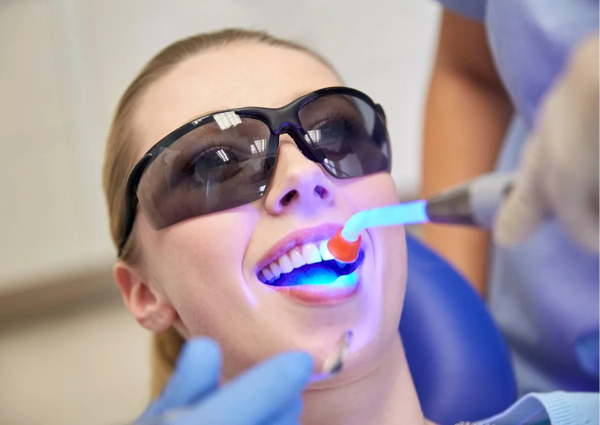 Dental professional curing tooth-colored bonding material with a blue light during a teeth bonding procedure.